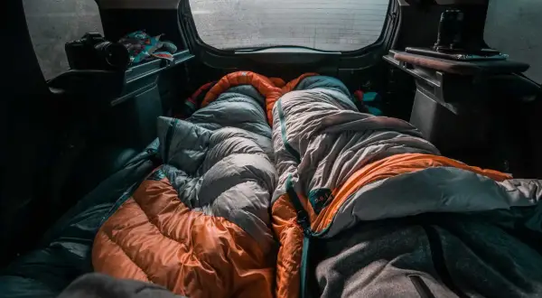 Gemütlich schlafen im Auto, zwei Schlafsäcke liegen bereit. Eine Kamera und Snacks sind auch da für das Abenteuer.