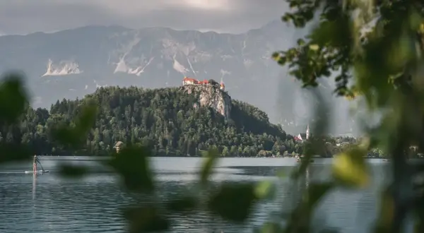 Jezioro Bled ze skalnym zamkiem, jedno z najpiękniejszych miejsc w Słowenii. Na pierwszym planie widać osobę na desce SUP.