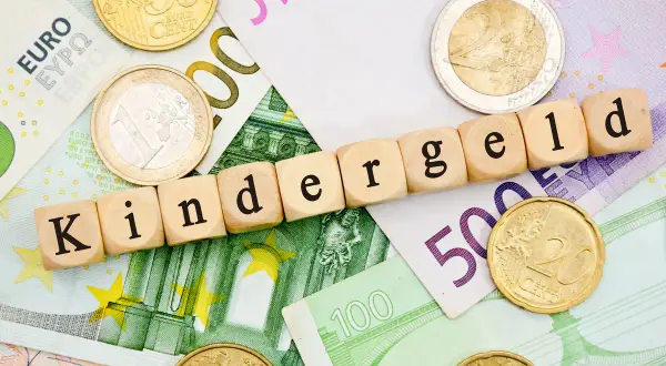 Drewniane klocki z napisem "Kindergeld" leżą na banknotach euro i monetach. Czekamy na Kindergeld 2026!