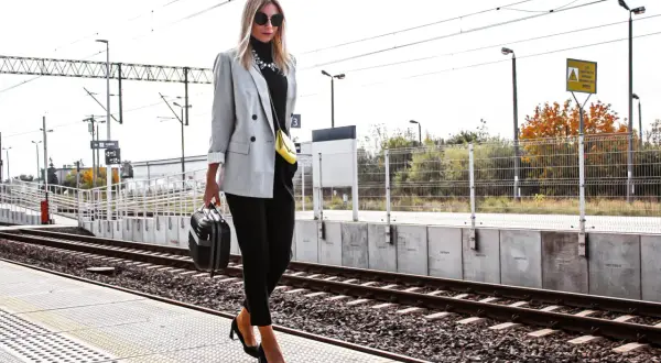 Elegancka szara marynarka damska w stylizacjach na podróż. Kobieta z małą walizką na peronie kolejowym.