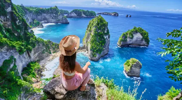 Vue imprenable sur la côte de Bali. Une femme assise au bord d'une falaise admire les îlots verdoyants et l'océan bleu. Idéal pour savoir que faire à Bali.