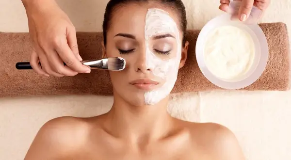 Una mujer recibe un tratamiento facial con una mascarilla aplicada con brocha.