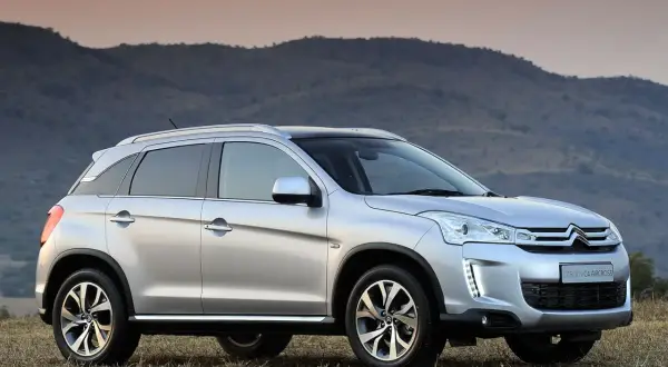 Srebrny Citroën C4 Aircross stoi na trawiastym wzgórzu, z górami w tle.