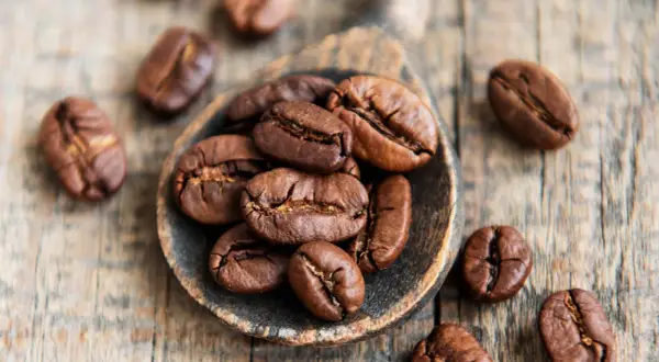 Chicchi di caffè tostati su un cucchiaio di legno, simbolo di alta qualità di caffè.