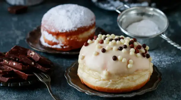 Dwa pączki: jeden oprószony cukrem pudrem, drugi polany lukrem i posypany kuleczkami. Pyszna pokusa, choć pączek kcal może przyprawić o zawrót głowy.