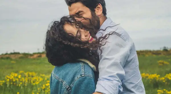 Un abbraccio intenso in un prato fiorito, un momento di pura comunicazione di coppia, dove sguardi e gesti parlano più delle parole.