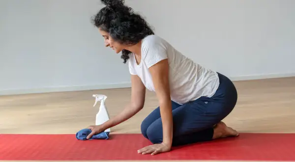 Frau reinigt ihre naturkautschuk yogamatte mit einem Tuch und Sprühflasche.
