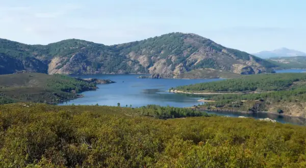 Paisaje sereno con un embalse azul rodeado de montañas verdes. La senda del Genaro se adentra en este idílico entorno natural.
