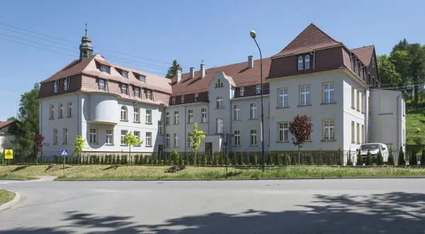 Elegancki budynek z wieżyczką, gdzie mieści się dom seniora Magda lenka, otoczony zielenią.