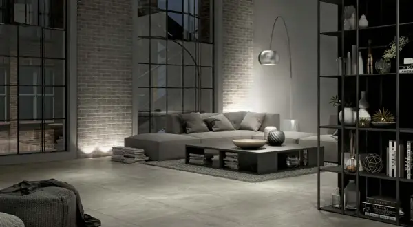 Salon industriel moderne avec canapé gris, table basse, étagères noires et **carrelage rectifié** au sol.