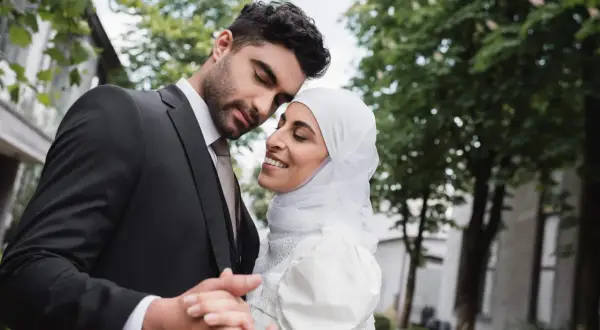 Un uomo in abito scuro e una donna con velo bianco si abbracciano teneramente, celebrando il loro matrimonio misto.
