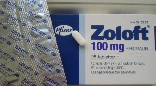 Opakowanie leku Zoloft 100 mg z sertraliną i blister z tabletkami.