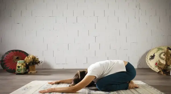 Mujer en postura de niño, buscando el yoga significado espiritual. Relajación y conexión interior.