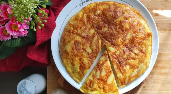A golden-brown potato frittata with a slice cut out, on a white plate with "Homemade" written on it.