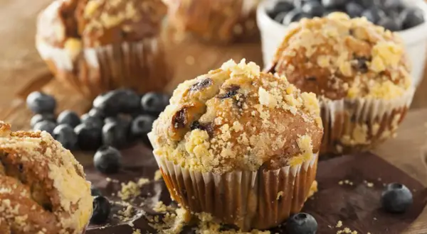 Frisch gebackene Blaubeermuffins mit Streuseln, ein köstliches Muffins Rezept, umgeben von frischen Blaubeeren.