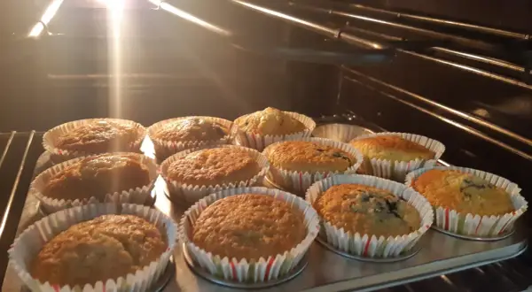 En plåt med nybakade glutenfria muffins i ugnen. Ljuset från ugnen lyser upp de gyllene muffinsarna.