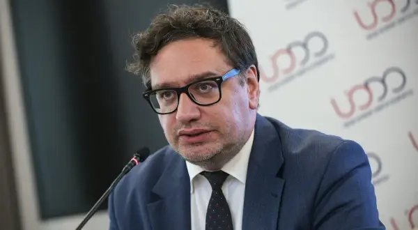 Mężczyzna w okularach i garniturze mówi do mikrofonu na tle logo UODO.
