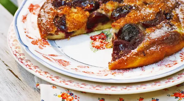 Ein goldbrauner Pfannkuchen mit Kirschen, bestreut mit Zucker, auf einem Teller mit Blumenmuster.