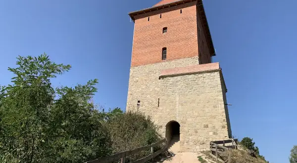 Wieża zamku Melsztyn z polską flagą na szczycie, kamienna podstawa i ceglana nadbudowa.