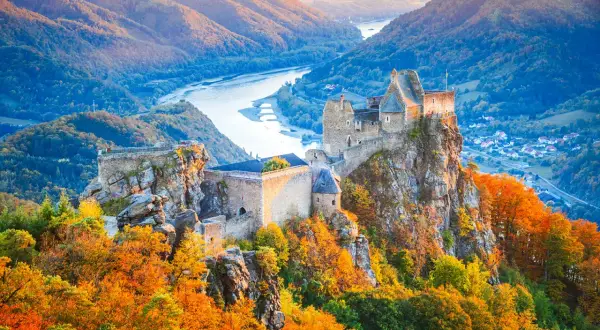 Zamek na skale w dolinie Wachau, otoczony jesiennymi barwami, z rzeką w tle.