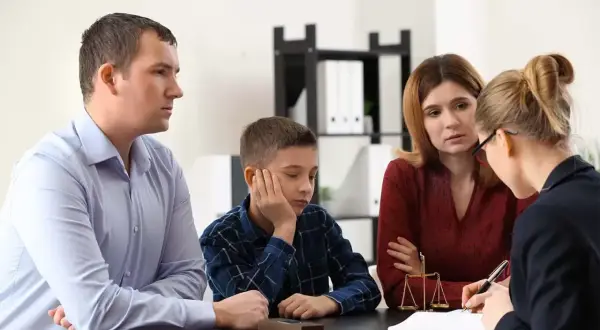 Rodzina z dzieckiem rozmawia z prawnikiem lub kuratorem sądowym. Na stole waga sprawiedliwości.