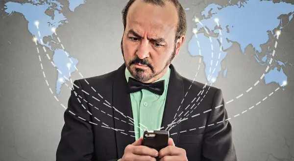 Mężczyzna w garniturze z kokardką patrzy na telefon, zastanawiając się, co to roaming i jak działa globalna sieć.