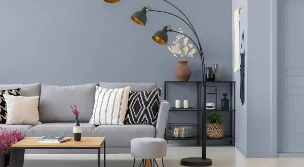 Nowoczesna lampa łukowa o ciemno szarym wykończeniu oświetla salon z szarą kanapą i stolikiem kawowym.