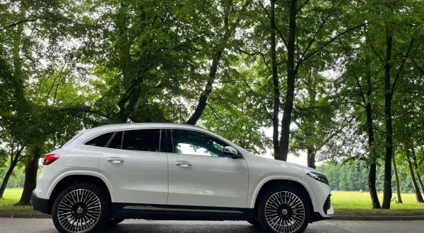 Biały Mercedes EQA stoi na tle zielonego, leśnego krajobrazu.