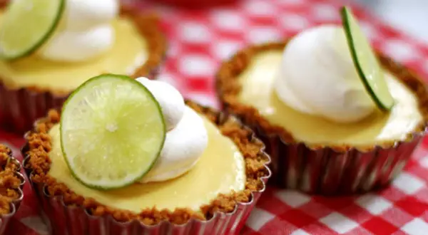 Små key lime pies med vispad grädde och limeklyfta på en rödvitrutig duk.