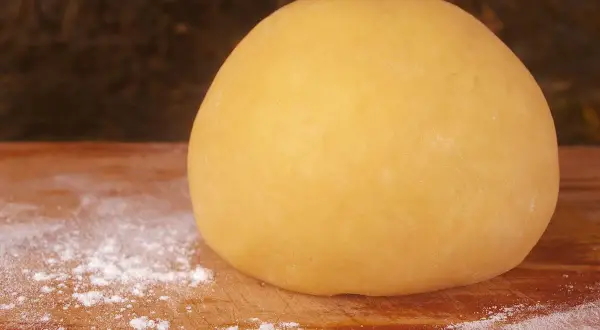 Impasto di pasta frolla per pastiera, 1 kg, pronto per essere steso su un tagliere infarinato.