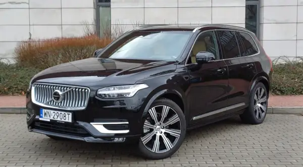 Elegancki, czarny Volvo XC90 z chromowanymi felgami stoi na brukowanym podjeździe.