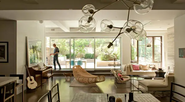 A man walks through a modern living room, captured in this interior architecture photography. A piano, guitar, and unique light fixture are visible.