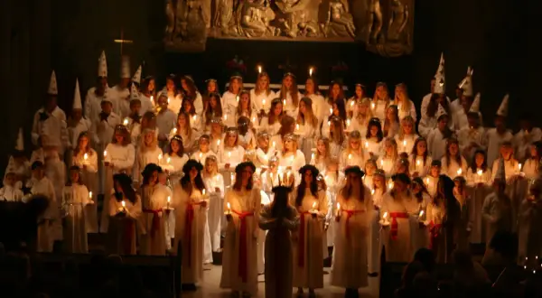 Ett stort kör av barn och ungdomar i vita dräkter och ljuskransar, som deltar i ett lucia firande i Stockholm.