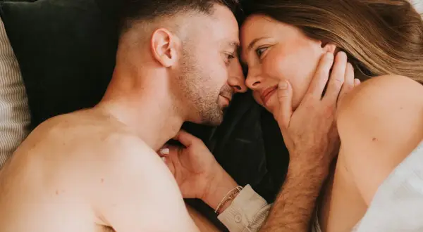 Un couple se regarde tendrement au lit. Ils semblent se retrouver après une période difficile, peut-être après une naissance et une épisiotomie, redécouvrant l'intimité.