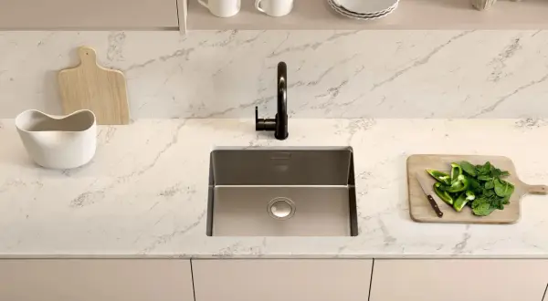 Plan de travail cuisine avec un évier en inox, un robinet noir, une planche à découper en bois avec des poivrons verts et des épinards, et une autre planche en bois.