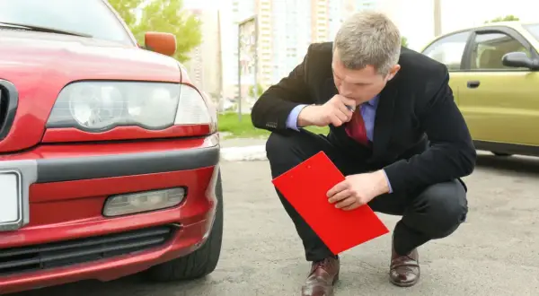 Man i kostym inspekterar en röd bil med en röd pärm, kanske för en digital servicebok.