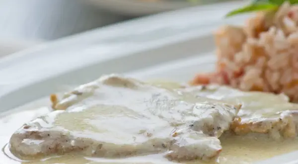 Zartes Putenschnitzel mit cremiger Rahmsauce, serviert mit einer Beilage aus Reis. Ein köstliches Gericht.
