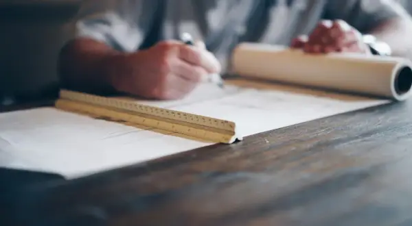 Architekt rysuje na planach, obok leży linijka i zwój papieru.
