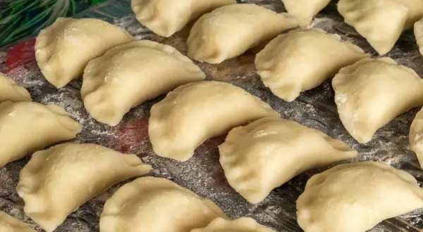 Gotowe do gotowania ciasto na pierogi, ułożone na desce, posypane mąką.