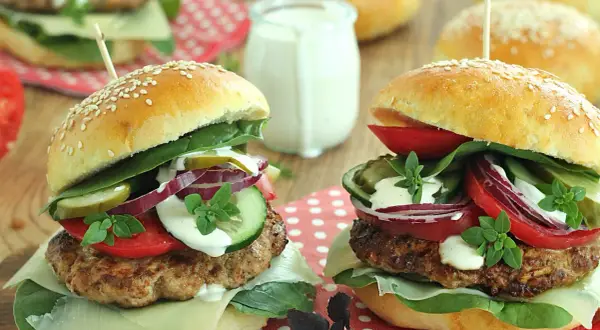 Dwa domowe burgery z serem, warzywami i sosem na drewnianym tle.