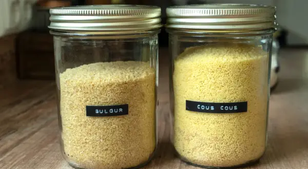Zwei Gläser mit Getreide: links Bulgur, rechts Couscous. Beide sind gut sichtbar und bereit für die Zubereitung.