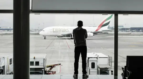 Mężczyzna w bluzie patrzy na samolot Emirates. Czeka na swój bagaż podręczny.