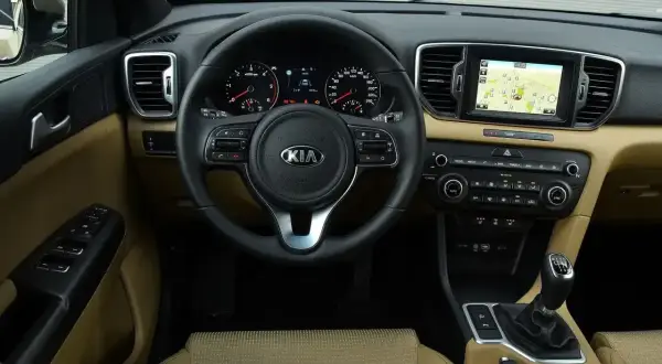 Wnętrze Kia Sportage IV z beżową tapicerką, multimediami z nawigacją i wielofunkcyjną kierownicą.