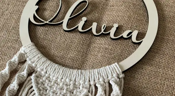 Un bel attrape-rêve personnalisé pour fabriquer un attrape rêve avec prénom. Le prénom "Olivia" est inscrit en lettres de bois sur un cercle orné de macramé.
