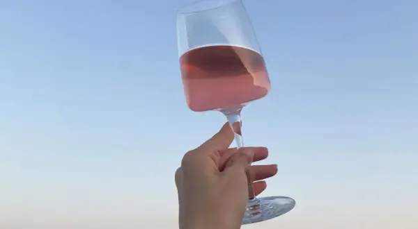 Różowe letnie wino w kieliszku, unoszone na tle błękitnego nieba. Idealny moment na orzeźwienie.