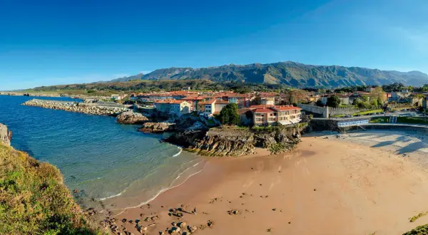 Costa asturiana con playa, pueblo costero y montañas. Descubre qué ver en Nueva de Llanes, un paraíso natural.