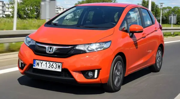 Pomarańczowy Honda Jazz w ruchu drogowym. Wiele osób szuka honda jazz opinie przed zakupem.