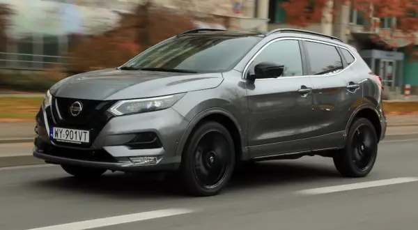 Szary Nissan Qashqai 2019 z czarnymi felgami pędzi ulicą, otoczony jesienną scenerią.