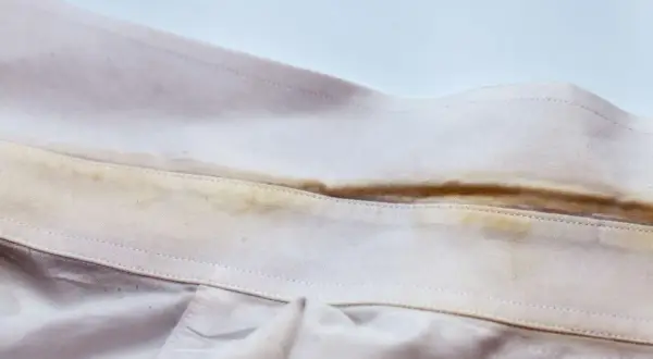 Colletto di camicia con evidenti macchie gialle, simili a quelle che si formano su asciugamani colorati dopo l'uso.
