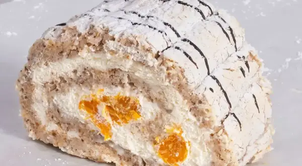 En bit Budapest bakelse med vispgrädde och aprikoser, pudrad med florsocker och dekorerad med choklad.